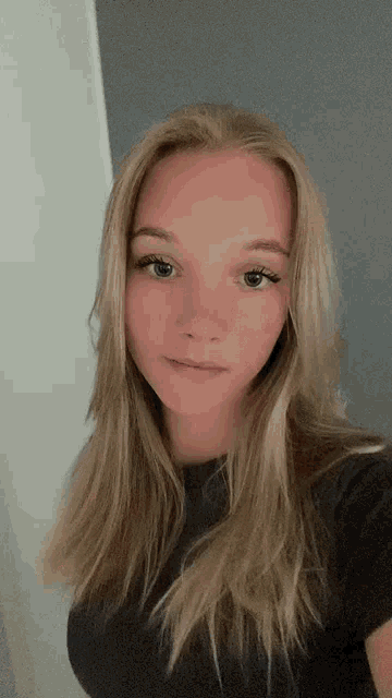 a young woman with long blonde hair is wearing a black shirt and looking at the camera .