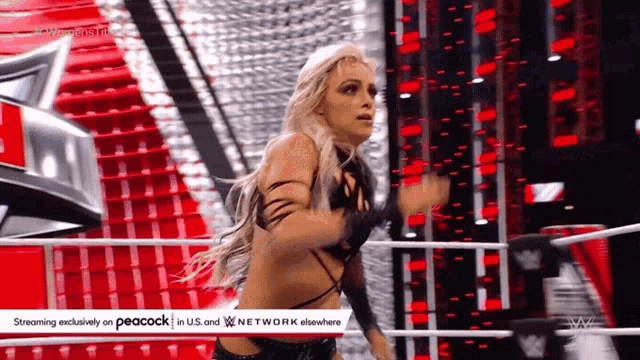 a woman is standing in a wrestling ring with a peacock logo in the corner .