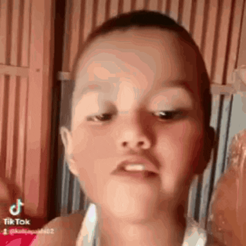a young boy with a shaved head is making a funny face while looking at the camera .