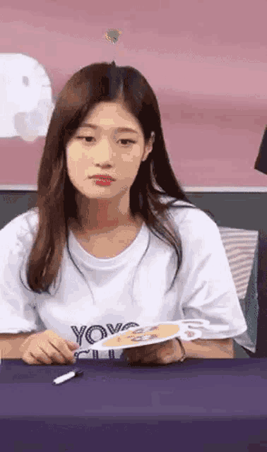 a woman is sitting at a table holding a fan and a pen .