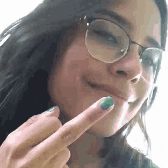 a girl wearing glasses and green nail polish is giving the middle finger