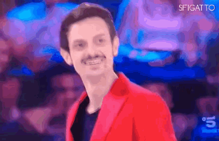 a man in a red jacket is smiling in front of a purple background with the letters sfigato on it