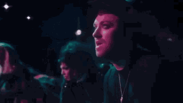 a close up of a man 's face in a dark room with a purple light behind him .