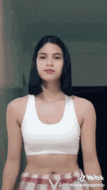 a woman in a white crop top and plaid shorts is standing in a room .