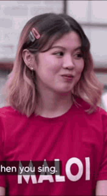a woman wearing a red shirt with the words `` when you sing , maloi '' on it is making a funny face .