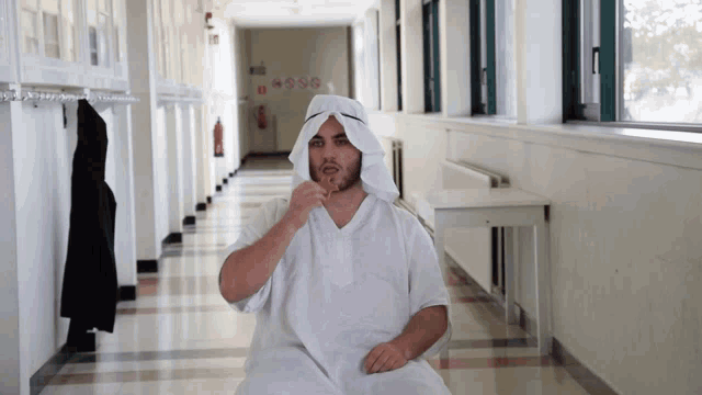 a man in a white robe is sitting in a hallway with the word sesso on the wall
