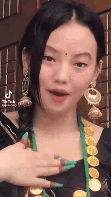 a tiktok video of a woman wearing earrings and a green necklace