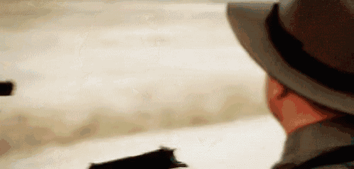 a man in a hat is holding a gun and pointing it .