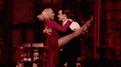 a man and a woman are dancing on a stage . the woman is wearing a red dress .