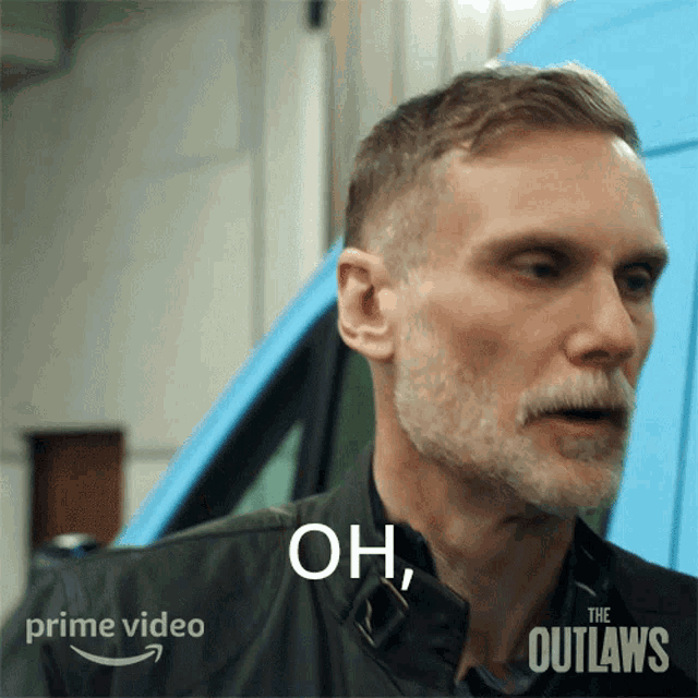a man with a beard is standing in front of a blue van with the words oh on his shirt