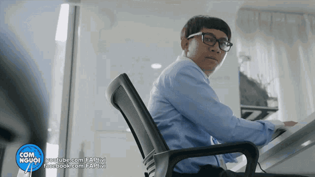 a man in a blue shirt sits at a desk in front of a youtube.com url