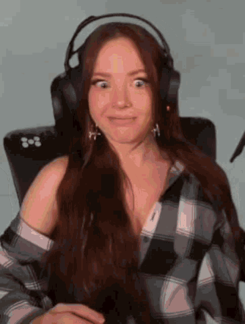 a woman wearing headphones and a plaid shirt is sitting in a chair and making a funny face .