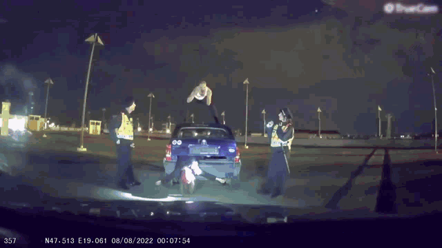 a police officer is standing next to a blue car with a man on the roof