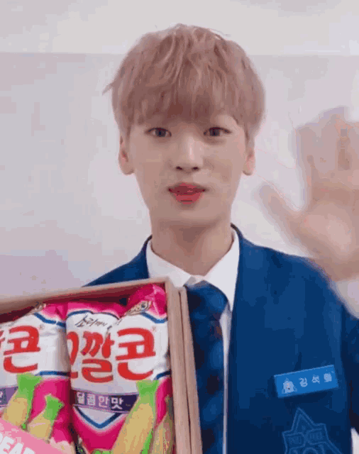 a young man in a blue suit and tie is holding a box of corn chips