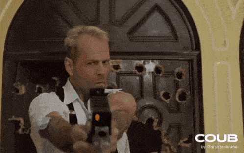 a man is pointing a gun in front of a door that has bullet holes