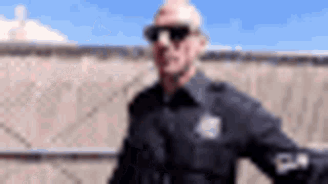 a police officer wearing sunglasses is standing in front of a fence .