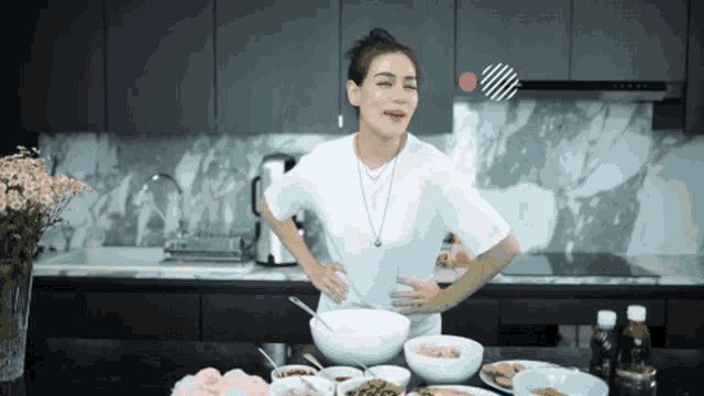 a woman in a white shirt is standing in front of a table with bowls of food