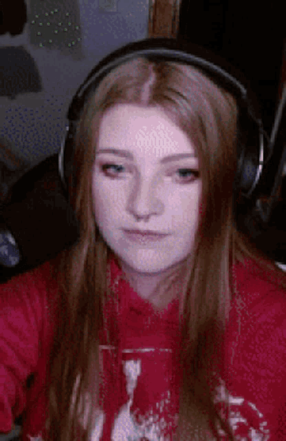 a woman wearing headphones and a red sweatshirt looks at the camera