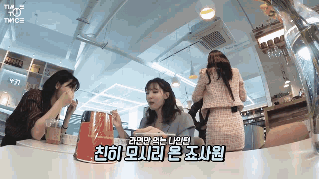 three women are sitting at a table and one of them is wearing a pink dress