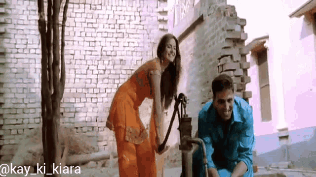 a man is pumping water from a well while a woman stands next to him