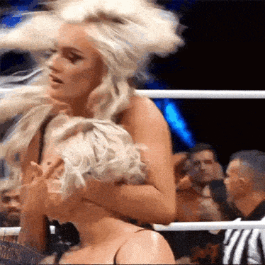 two blonde women are wrestling in a ring with a referee watching .