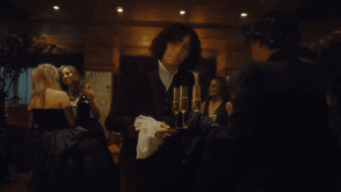 a group of people are gathered in a dark room with a man holding a glass of wine