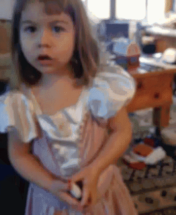 a little girl in a pink and white dress is standing in front of a messy desk
