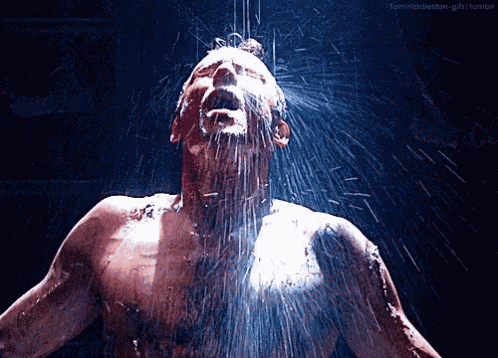 a shirtless man is taking a shower with water spraying on his head