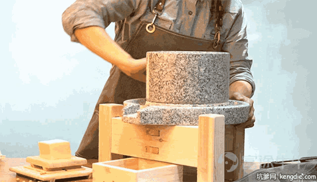 a person in an apron is using a stone grinder with the website kengdie.com in the background