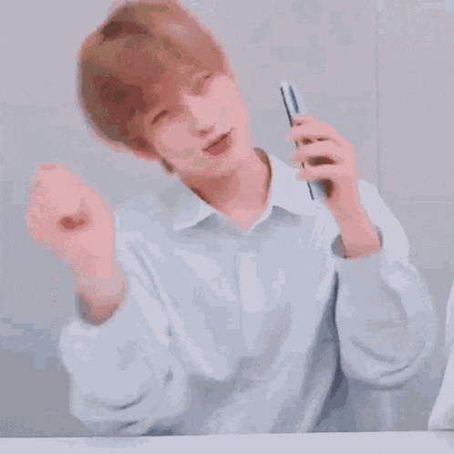 a young man in a white shirt is sitting at a table holding a pen .