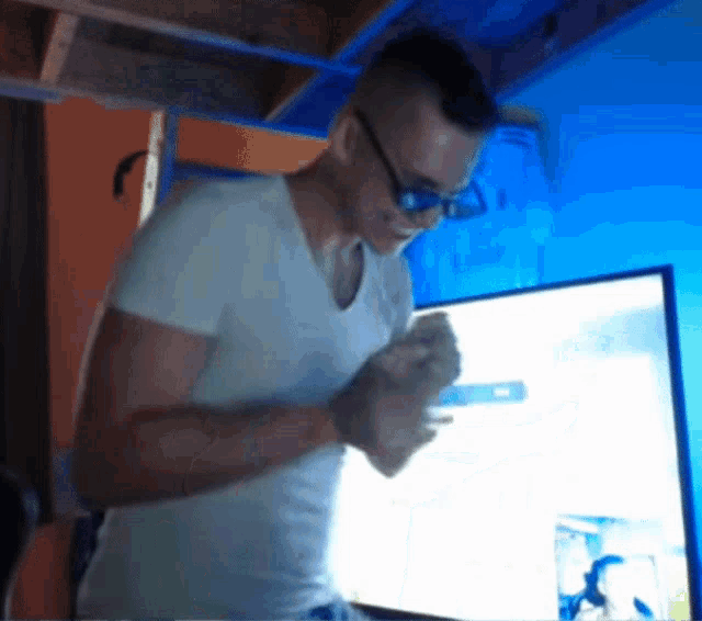 a man wearing glasses and a white shirt is standing in front of a tv
