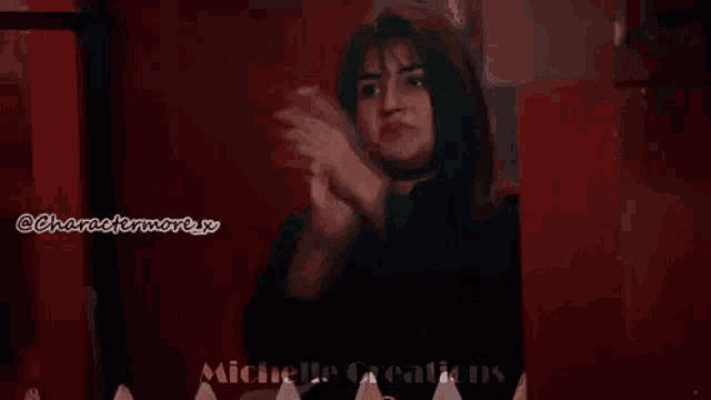 a woman is standing in front of a red wall with her hands up .