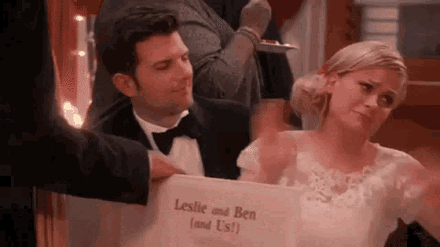 a bride and groom are sitting at a table with a sign that says leslie and ben and us