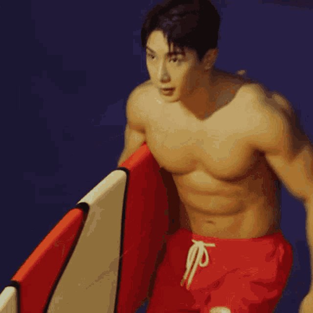 a shirtless man carrying a red and white surfboard on a blue background