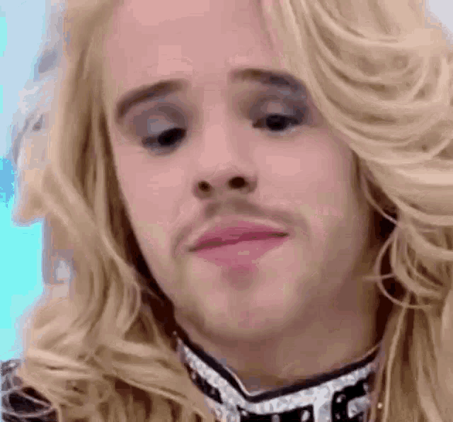 a man with long blonde hair and a beard is wearing a wig and makeup .