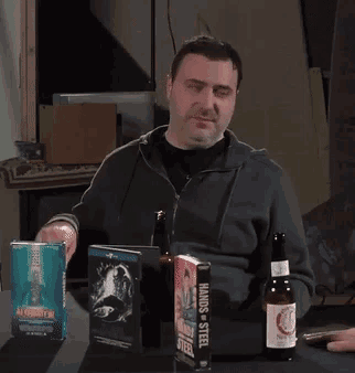 a man is sitting at a table with a bottle of beer and a book called hands of steel