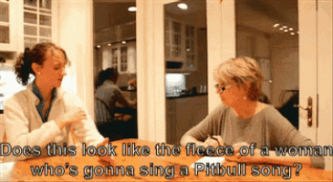 two women are sitting at a table and one of them is singing a pitbull song ..