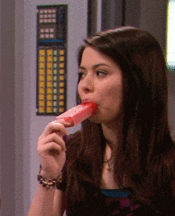 a girl is eating a pink popsicle in front of a wall with buttons on it