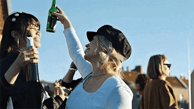 a woman is holding a bottle of beer in her hand while another woman looks on .