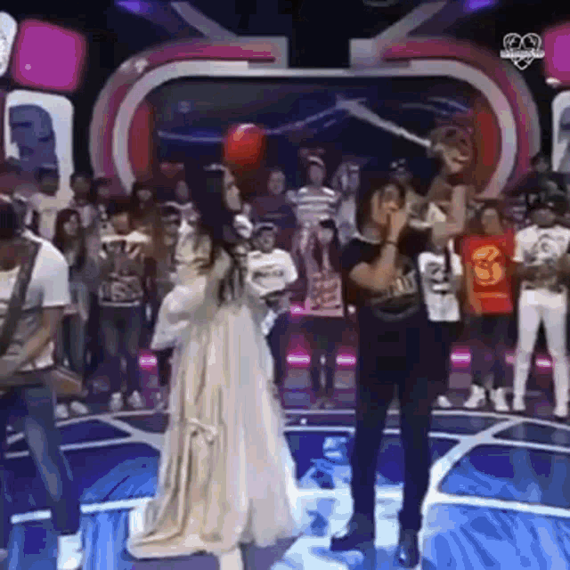 a woman in a white dress is standing in front of a crowd on a stage holding a balloon .
