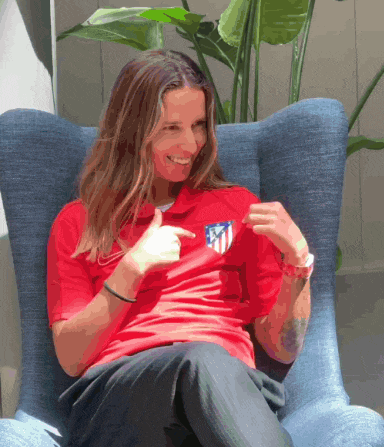 a woman is sitting in a chair wearing a red shirt that says atlético madrid