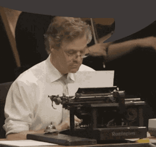 a man in a white shirt and tie is typing on a remington brand typewriter