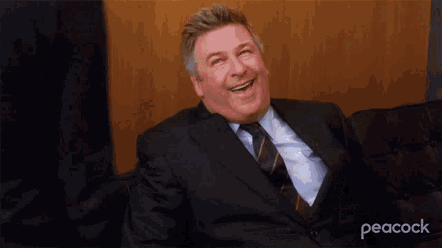 a man in a suit and tie is laughing while sitting on a couch ..
