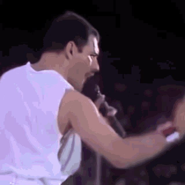 a man is singing into a microphone while wearing a white tank top .