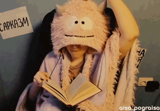 a person wearing a stuffed animal hat reads a book