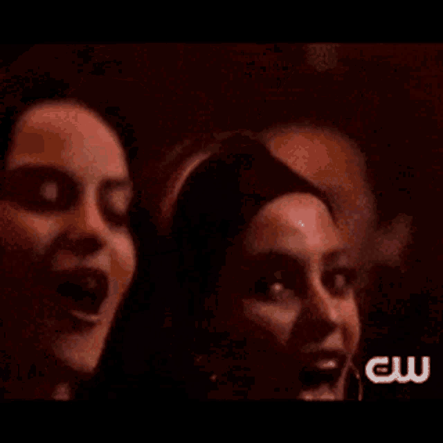 two women are standing next to each other in a dark room and smiling .