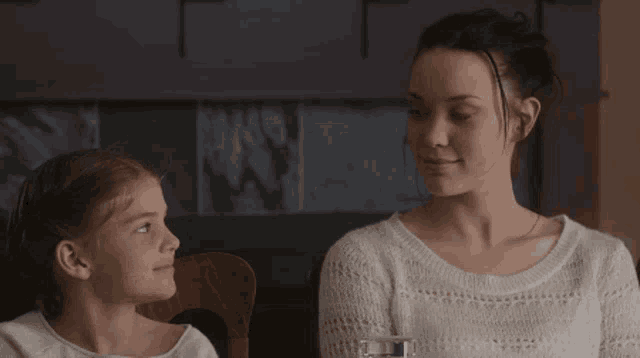 a woman and a little girl sit at a table with a glass of water
