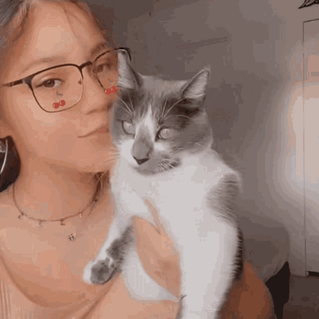 a woman wearing glasses is holding a cat