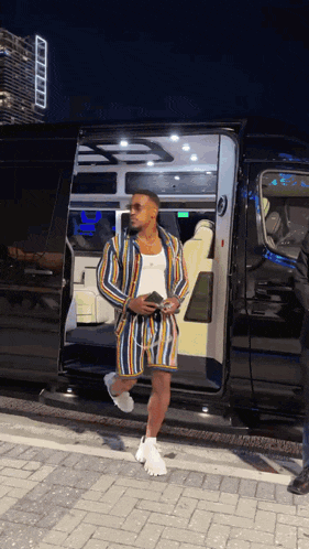 a man in a striped jacket and shorts is getting out of a black van