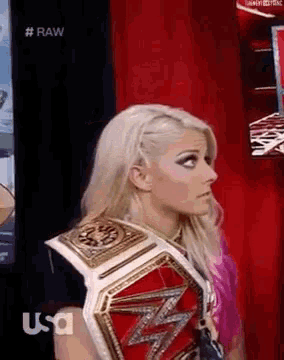 a woman wearing a wrestling championship belt is standing in front of a red curtain .